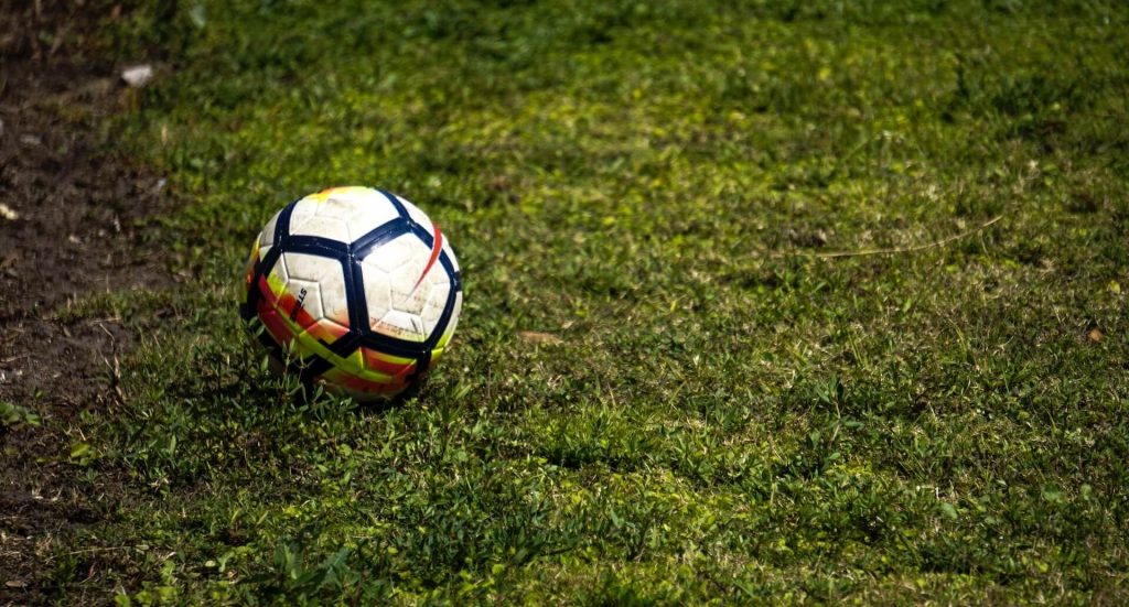Un balón de fútbol cubierto de barro tendido en un campo de fútbol embarrado, reflejando la intensidad y la fisicalidad del juego