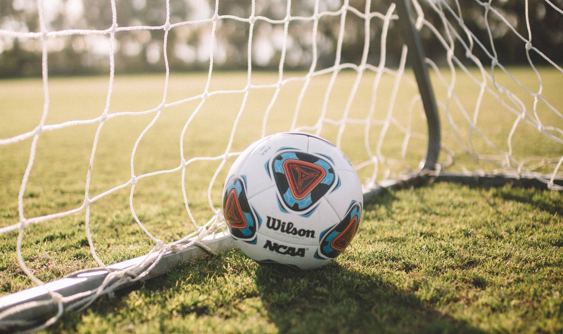 Un balón de fútbol encajado dentro de la red de una portería, simbolizando un gol acertado.