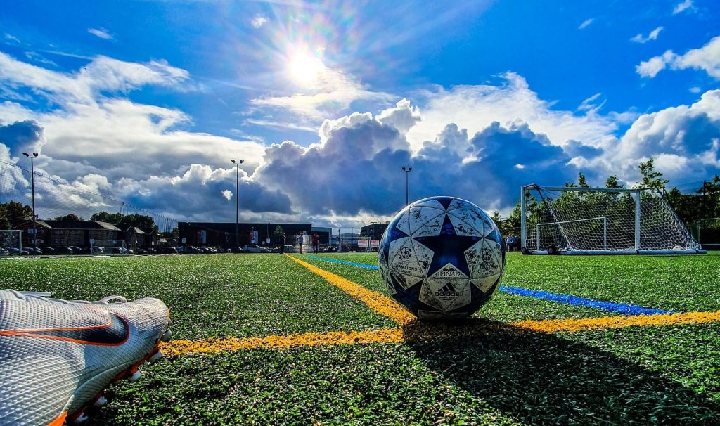 Un campo de fútbol vibrante con un balón en movimiento bajo el sol brillante, capturando la energía de un partido en curso